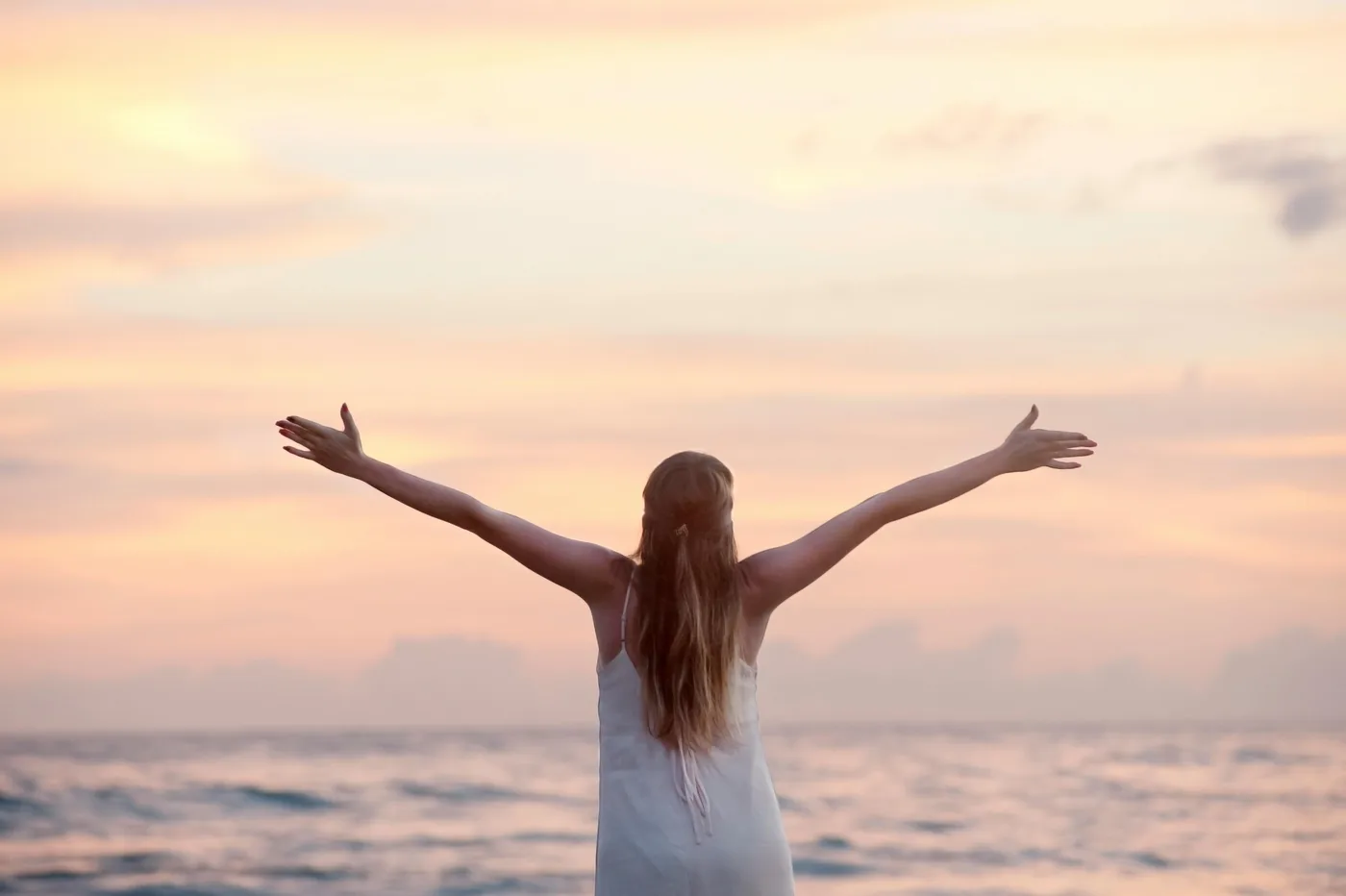 Femme debout face à la mer, bras ouverts, au coucher du soleil